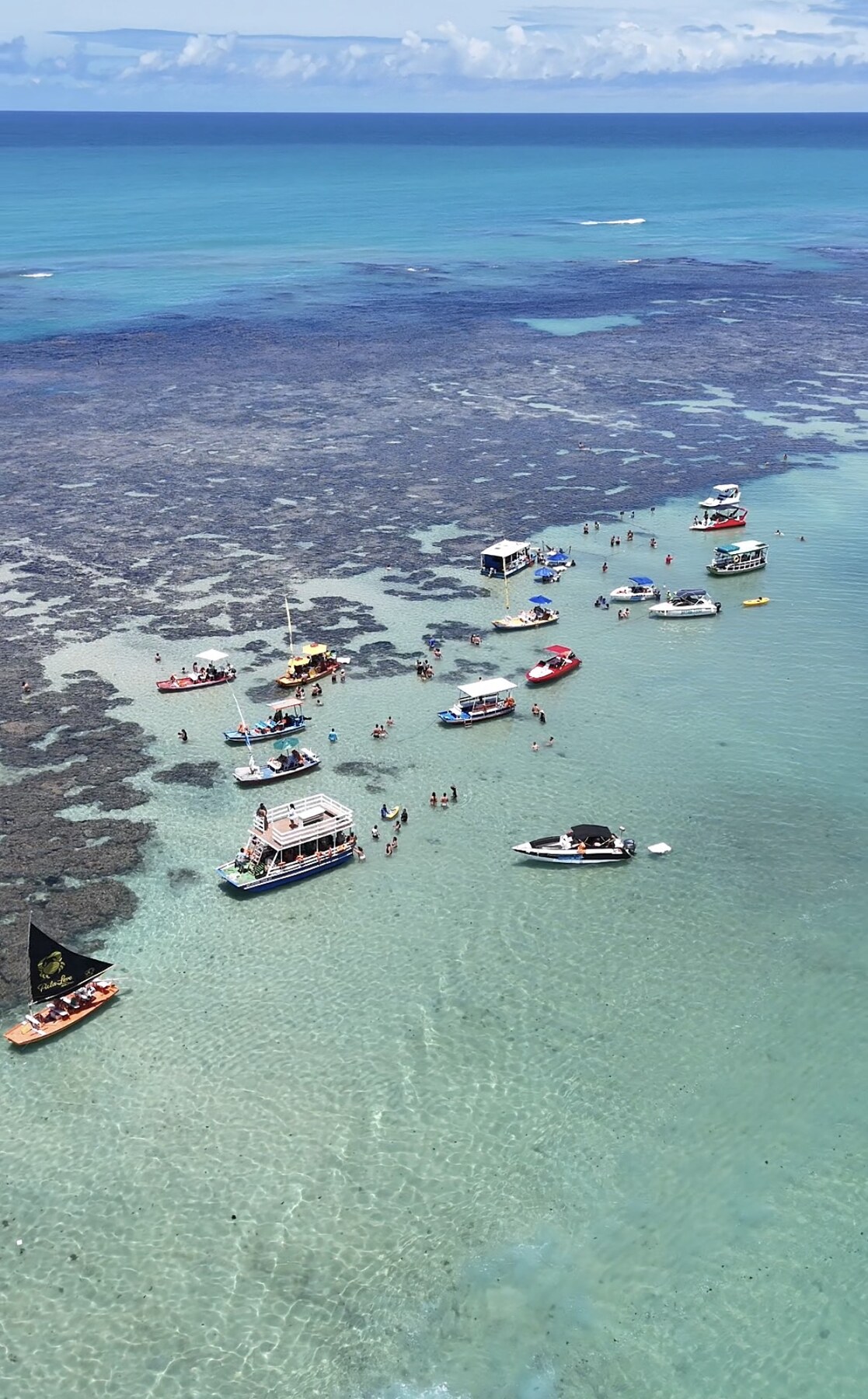 Vista aérea diagonal das piscinas naturais de Pajuçara com barcos e banhistas