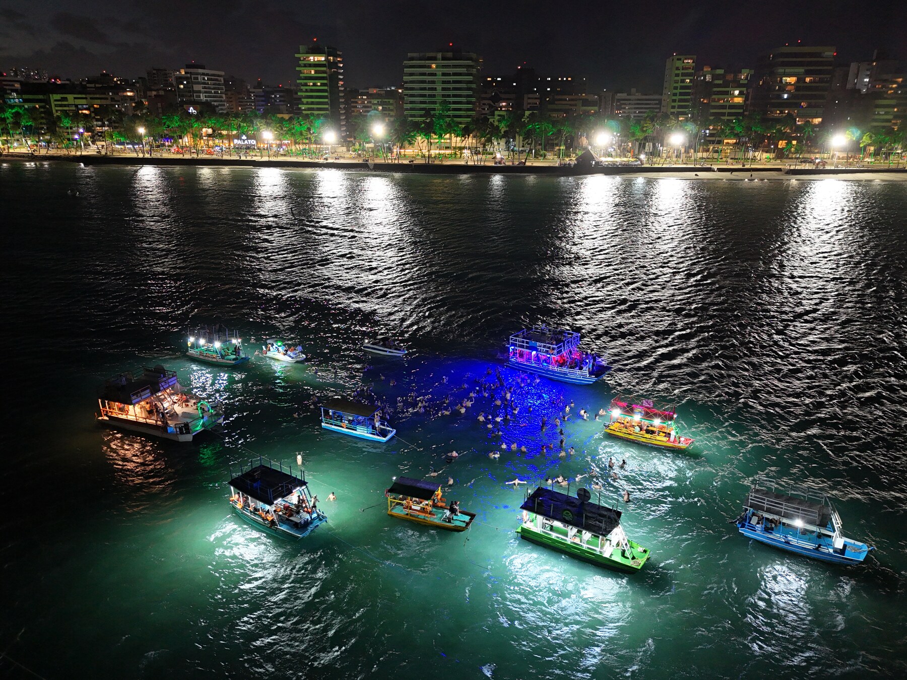 Vista aérea panorâmica do banho de lua em Maceió com luzes coloridas refletindo no mar noturno